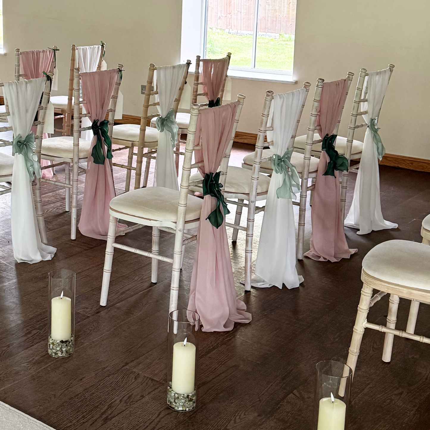 Decorated chairs with pink and white ribbons on a wooden floor.