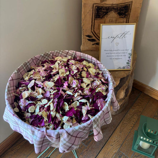 Basket of colourful flower petals in a basket with pink tartan on a wooden floor with a decorative sign in the background.