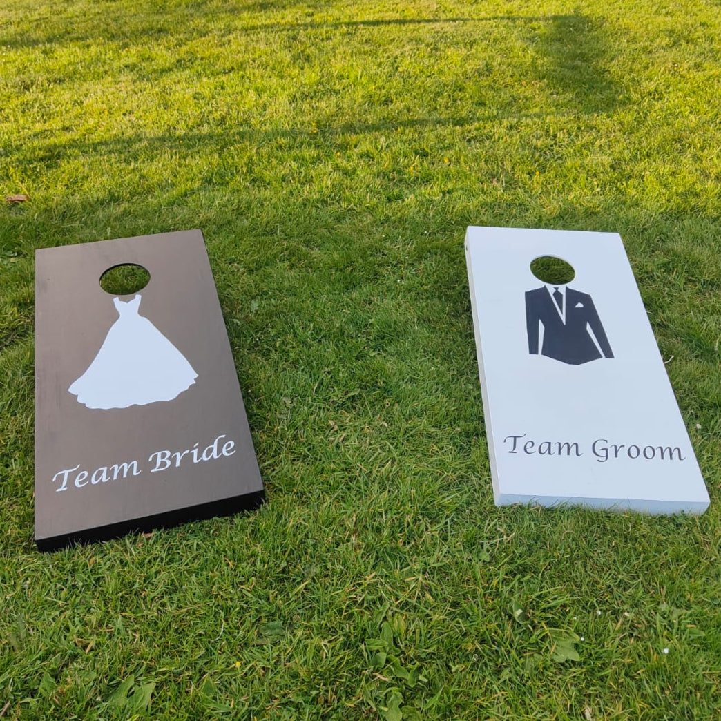 Cornhole boards labeled 'Team Bride' and 'Team Groom' on a lawn.