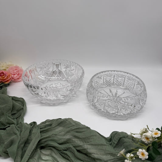 Two crystal bowls with floral and cheesecloth fabric on a light background and flowers on the left hand side.