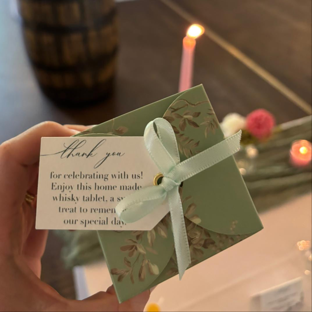 Hand holding a favour box with a tag in a room with candles and flowers