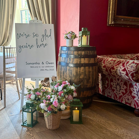 Decorative setup with flowers, candles, and a sign on a wooden floor.