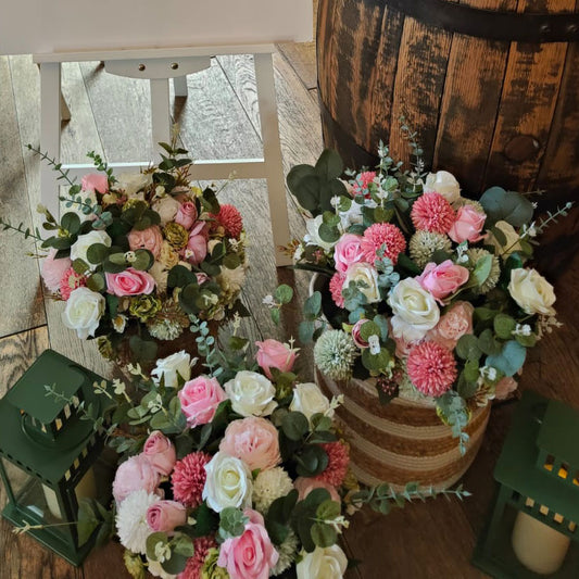 Three floral arrangements in front of a wooden barrel with lanterns on a wooden floor.