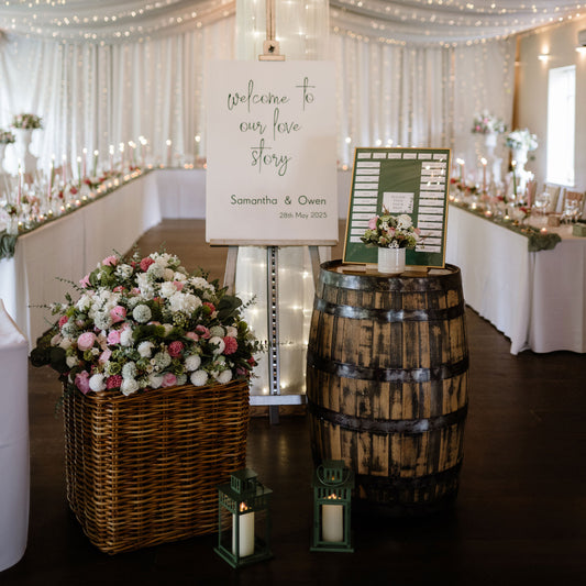 Decorative setup with flowers, barrels, and a sign in a wedding venue.