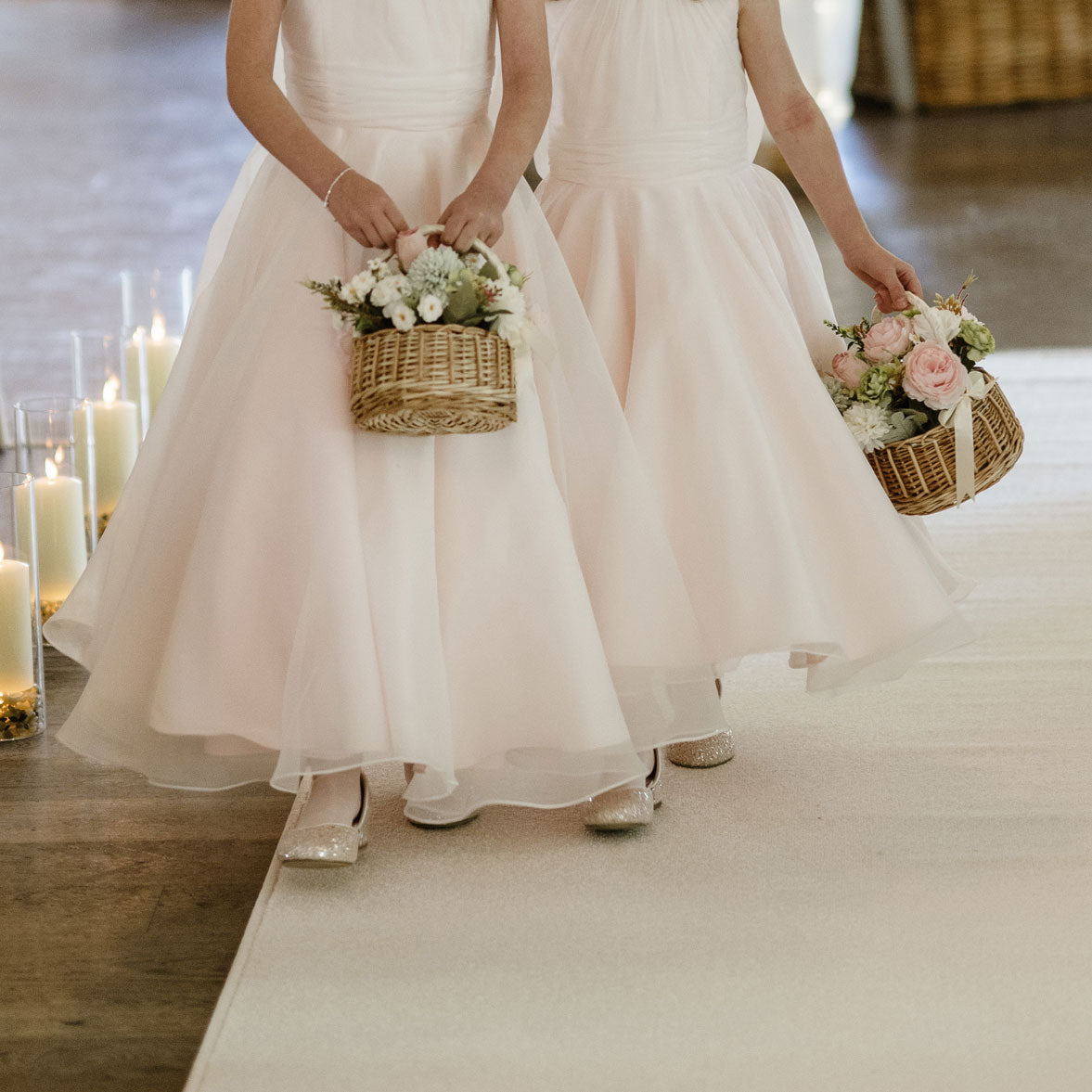 Two flower girls in white dresses holding flower baskets on a white aisle runner.