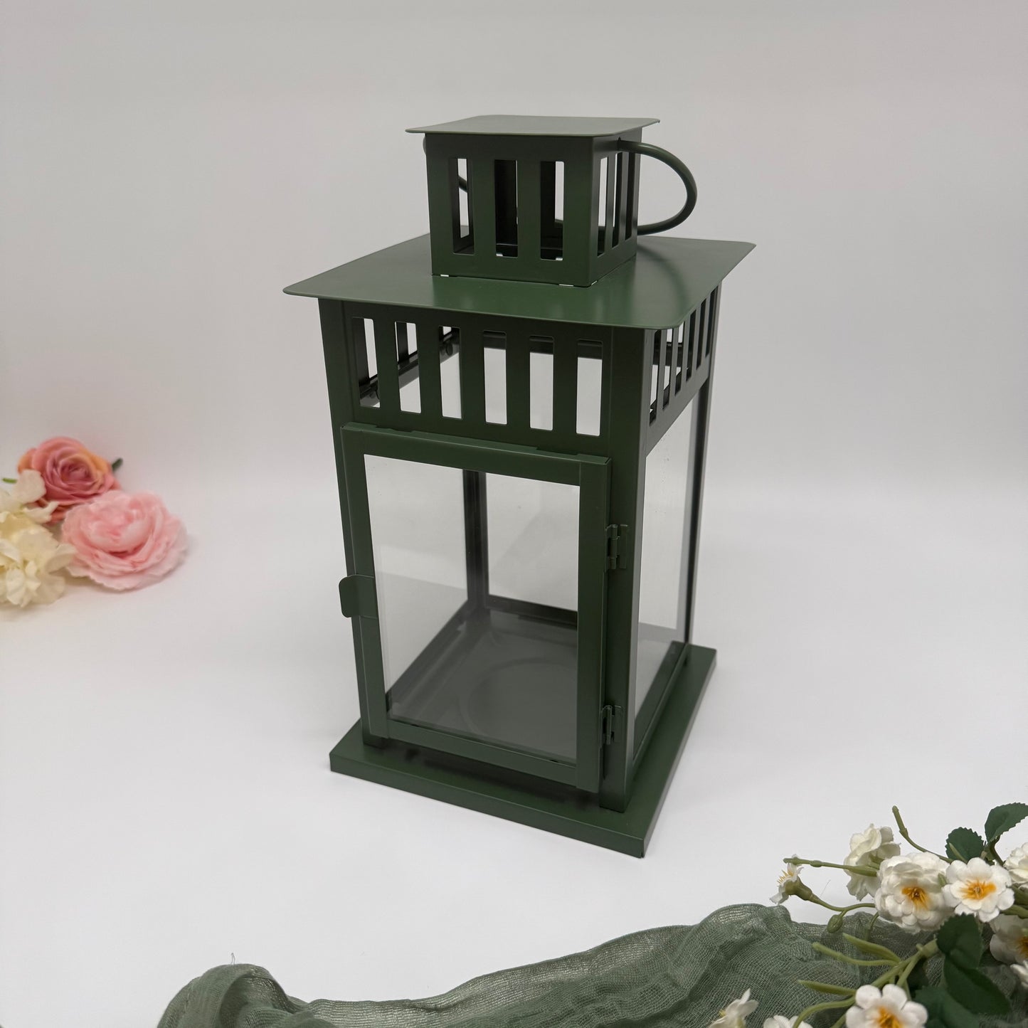 Green metal lantern, surrounded by flowers on a white background