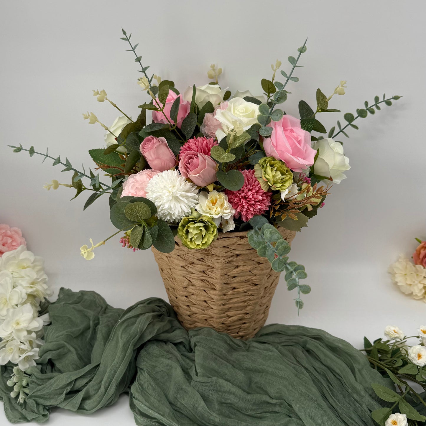 Bouquet of flowers in a woven basket on a green fabric with a plain background