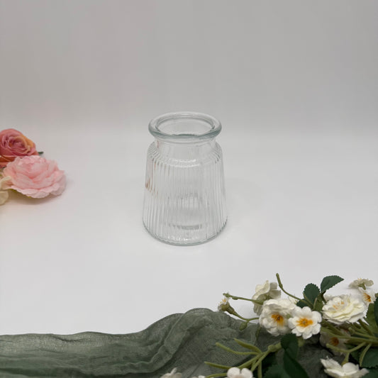 Small textured glass vase with subtle flowers around it on a white background