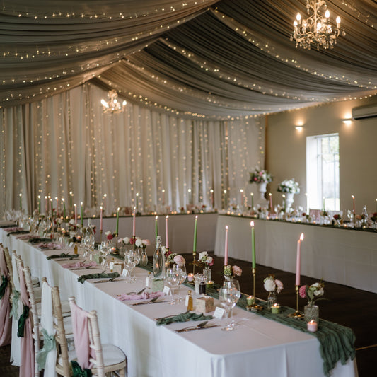 Decorated wedding space with tables set for a meal, string lights, and a chandelier.