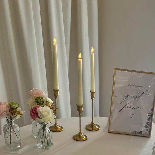 Decorative setup with candles on brass candlesticks, flowers in bud vases, and a framed sign on a table.