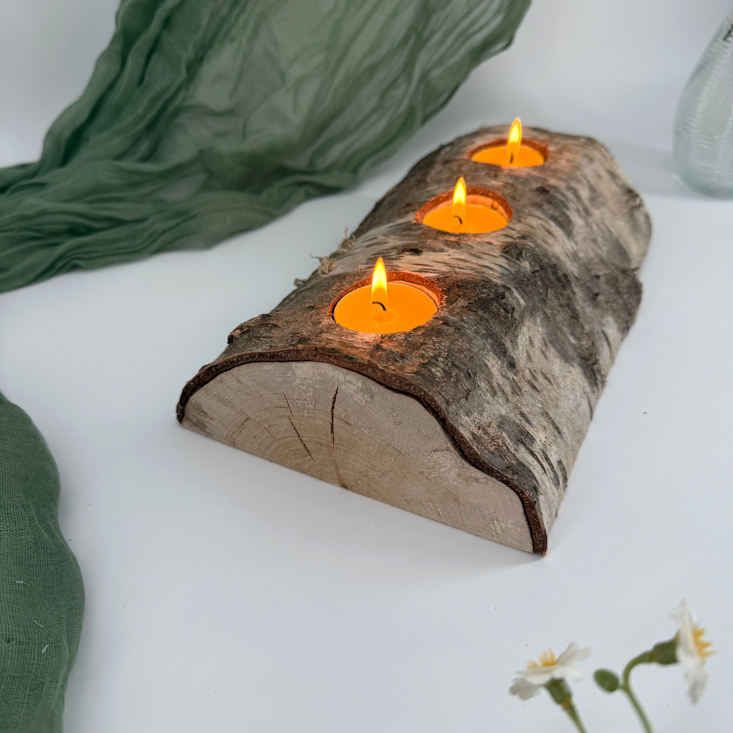 Candle holder made of a wooden log with three lit candles on a white surface.