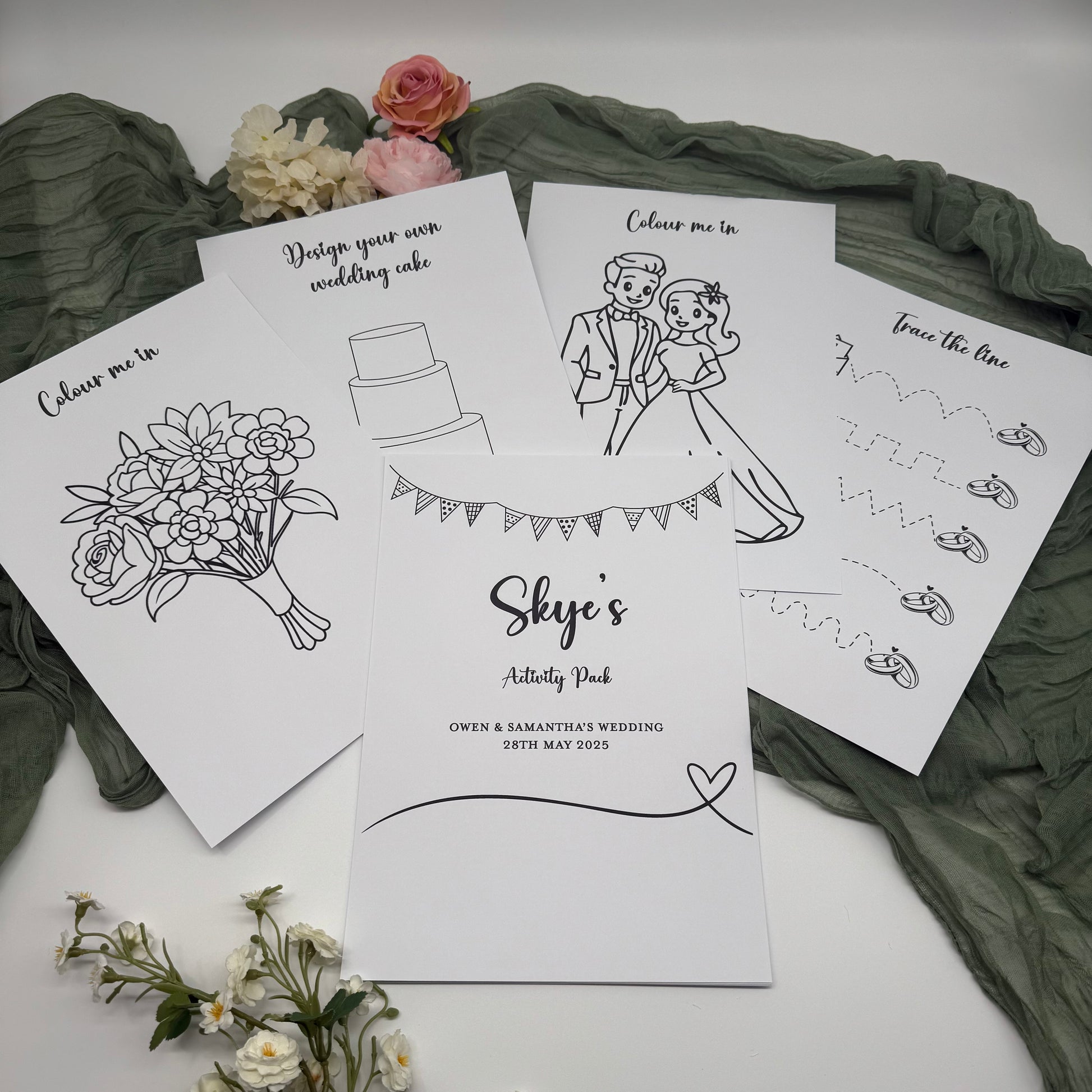 Children's wedding activity pack with colouring pages on a white surface with green fabric and flowers.