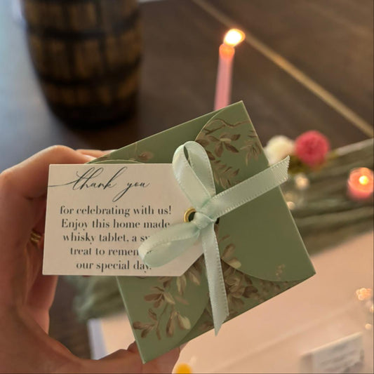 Hand holding a favour box with a tag in a room with candles and flowers