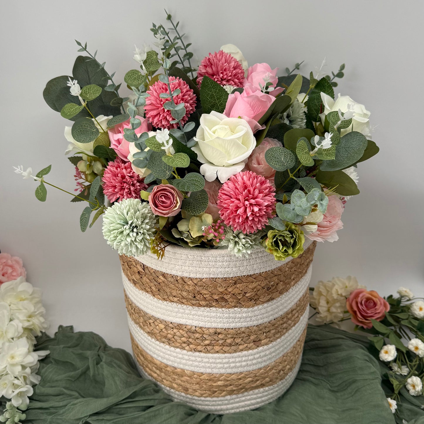 Bouquet of pink, white, and green flowers in a woven basket on a light gray background.
