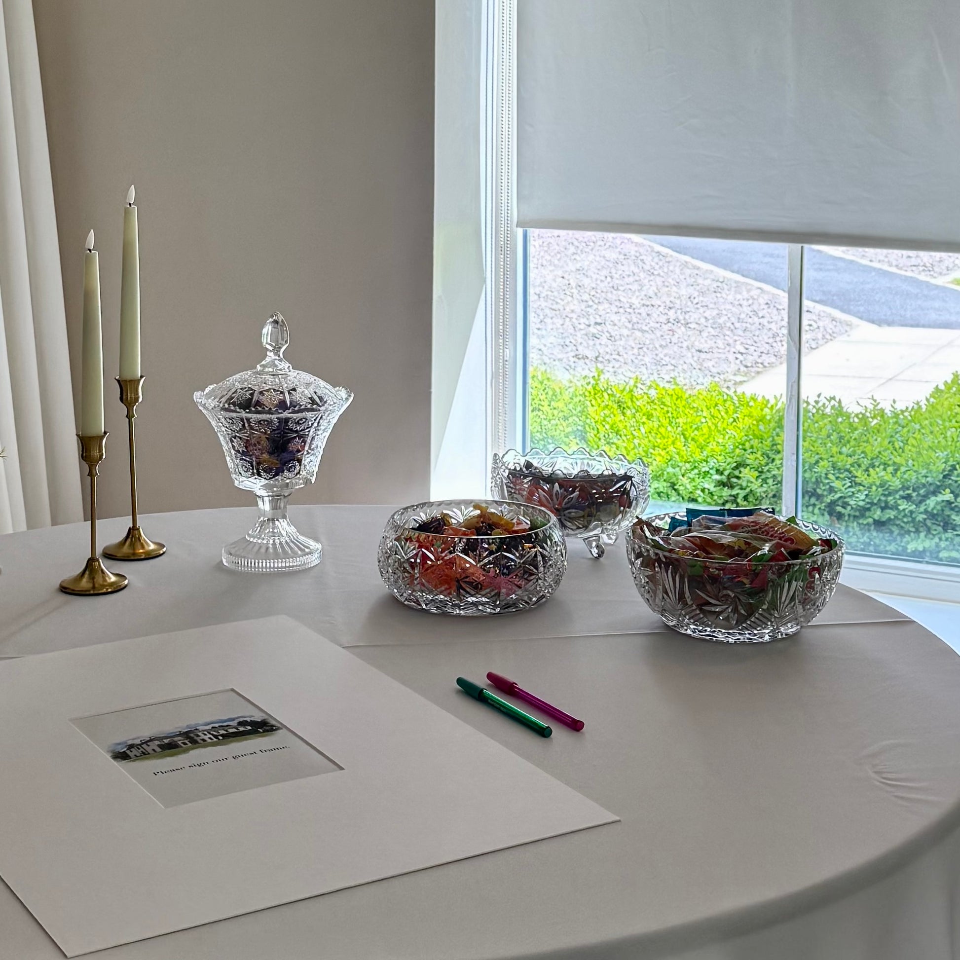Decorative glass bowls filled with sweets on a table with a scenic view outside a window.