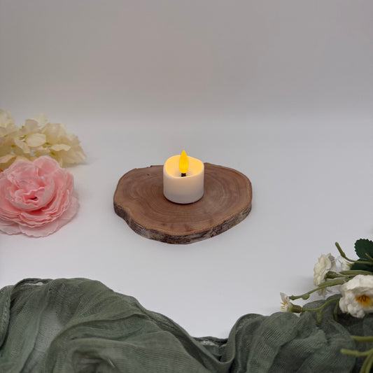 LED Tea light sitting on wooden coaster with flowers to the left