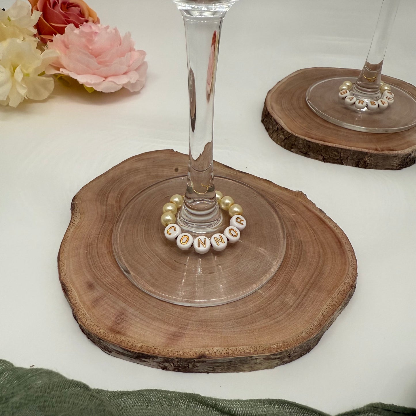 Wooden coaster with a glass and decorative beads on a white surface with flowers.