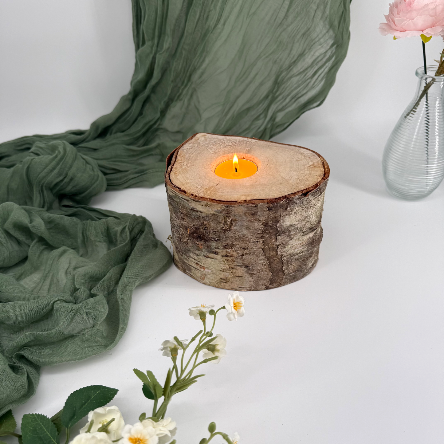 Candle in a wooden holder with green fabric and flowers on a white background